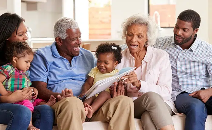 Multigenerational family sitting on a couch, reading a book together and smiling.