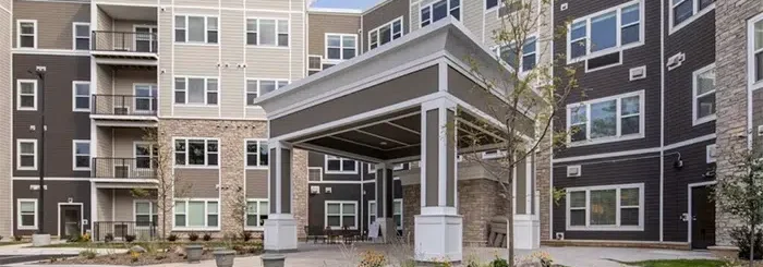 Modern multi-story apartment building with a covered entrance and landscaped front yard.